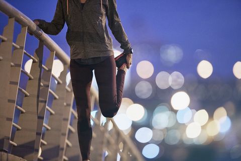 Female runner stretching leg on footbridge at dusk