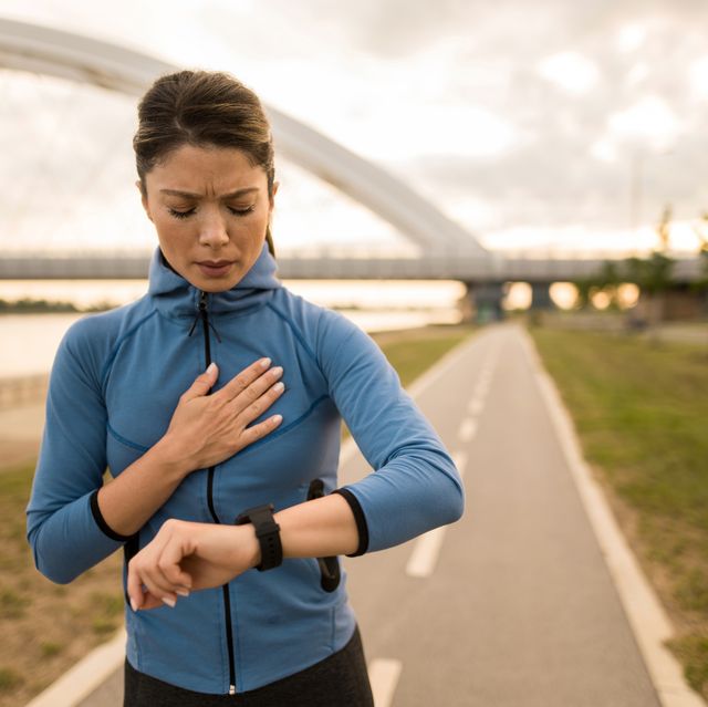 exhausted athletic woman looking at smart watch while exercising outdoors in the morning.