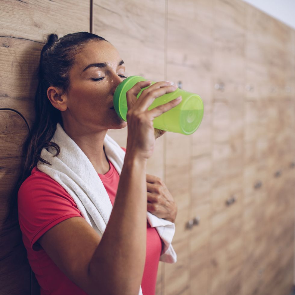 Exhausted woman drinking water in locker room after sports training.