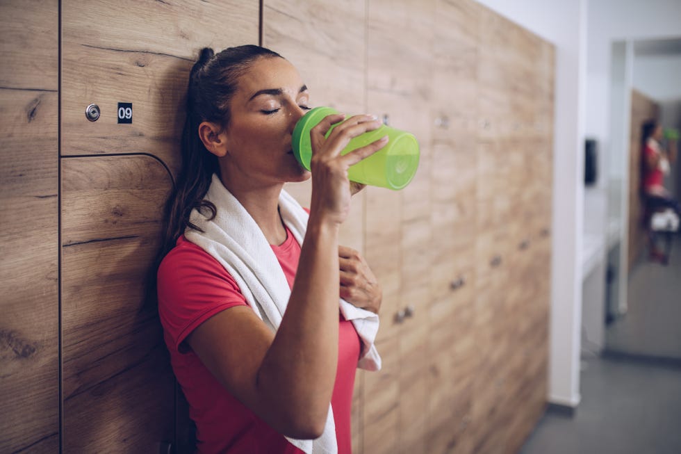 Exhausted woman drinking water in locker room after sports training.