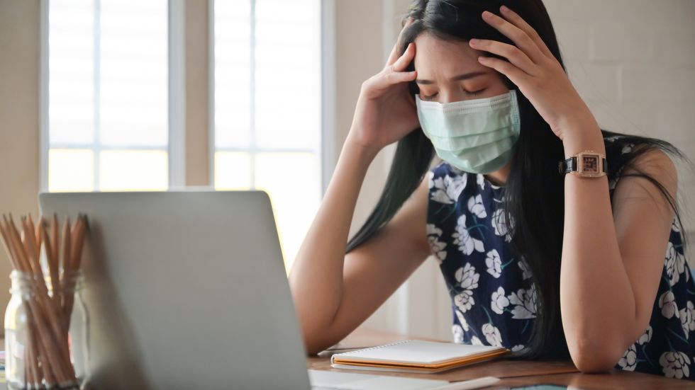 exhausted woman wearing mask using laptop at home