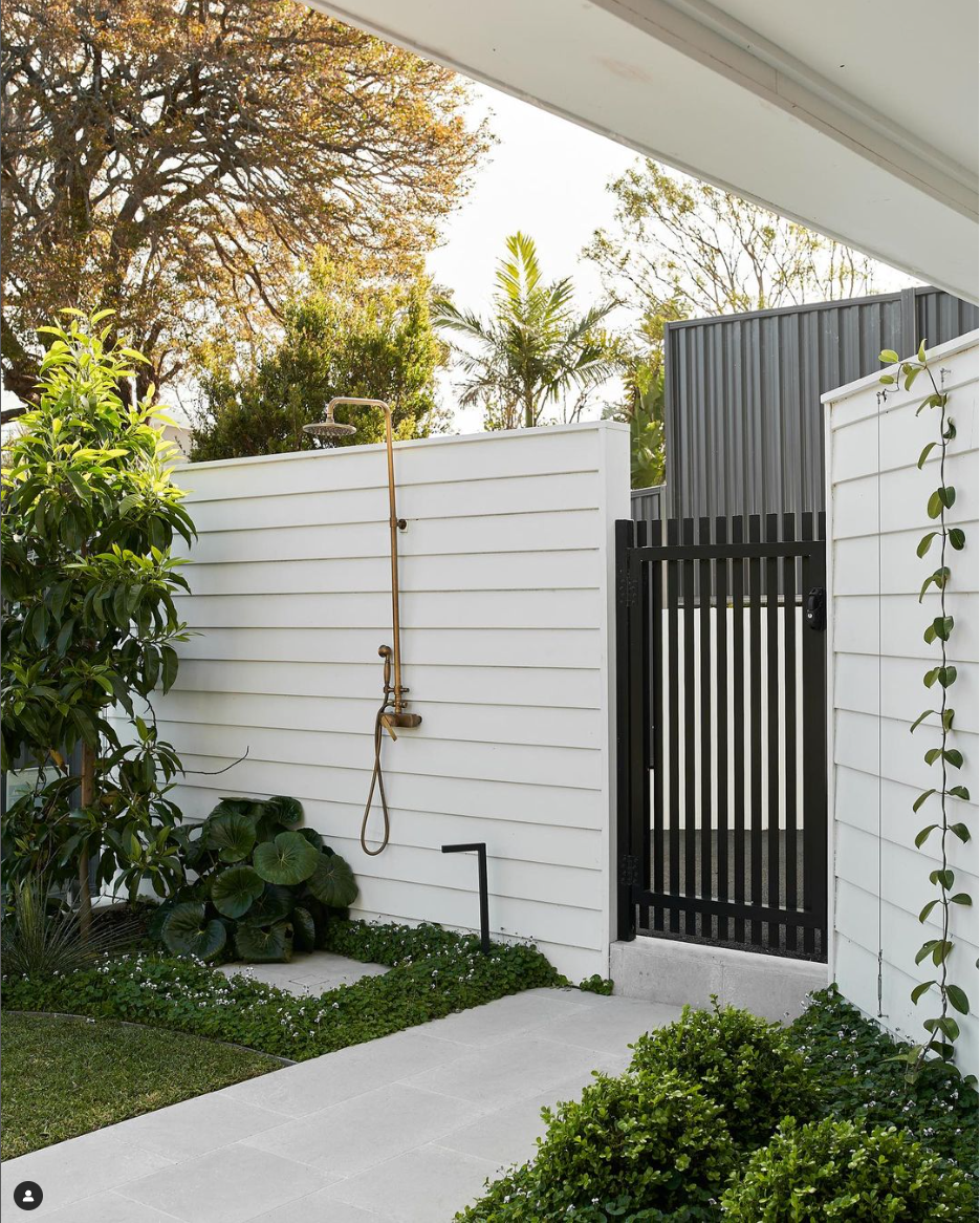 a brass outdoor shower fixture next to black gate