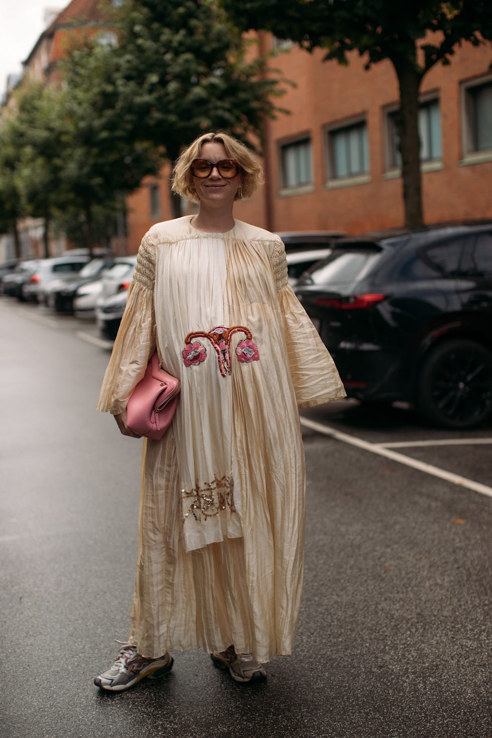 fashionable individual with blonde very short bob in a long cream dress holding a pink handbag bob haircut copenhagen fashion week