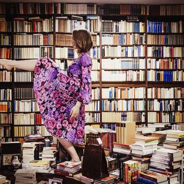 exuberant woman dancing on book stacks in library