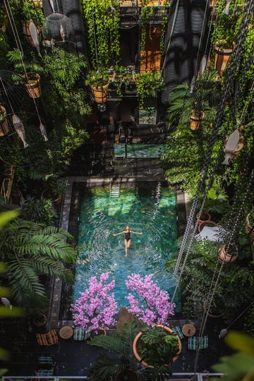 a woman floating on her back in a bali inspired pool with palm trees and colorful flowering trees surrounding its perimeter