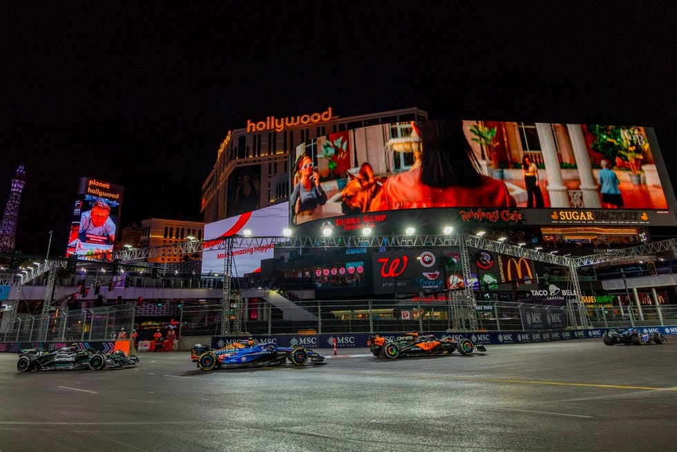 a group of race cars on a road with a large billboard