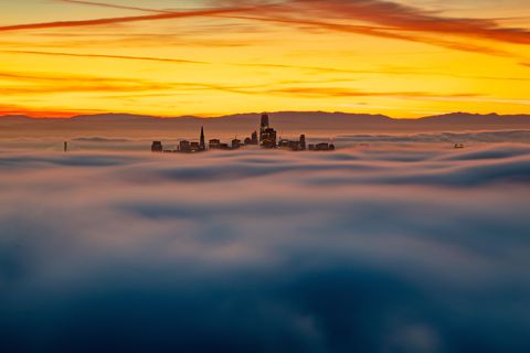 Alleen de toppen van de hoogste gebouwen van San Francisco zijn zichtbaar boven de mist en worden verlicht door een spectaculaire zonsopgang Wat een magische ochtend was dit herinnert Your Shotfotograaf Aya Okawa zich