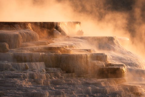 Tijdens mijn reizen zijn er plekken die tijdens verschillende momenten van de dag heel andere gedaanten aannemen zegt Your Shotfotograaf Garrine Tsang Zo ook bij Canary Spring onderdeel van het Main Terrace in Mammoth Hot Springs in Yellowstone De periodieke ontlading van de heetwaterbron en de koele ochtendlucht zorgen ervoor dat de stoom en thermische activiteit prominenter aanwezig zijn tijdens de dageraad