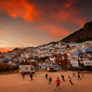 De ondergaande zon schijnt over een groep kinderen die voetballen in Chefchaouen in Marokko Op de achtergrond ziet je enkele van de beroemde blauwe huizen die Chefchaouen de bijnaam The Blue City geven