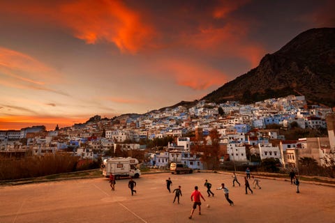 De ondergaande zon schijnt over een groep kinderen die voetballen in Chefchaouen in Marokko Op de achtergrond ziet je enkele van de beroemde blauwe huizen die Chefchaouen de bijnaam The Blue City geven