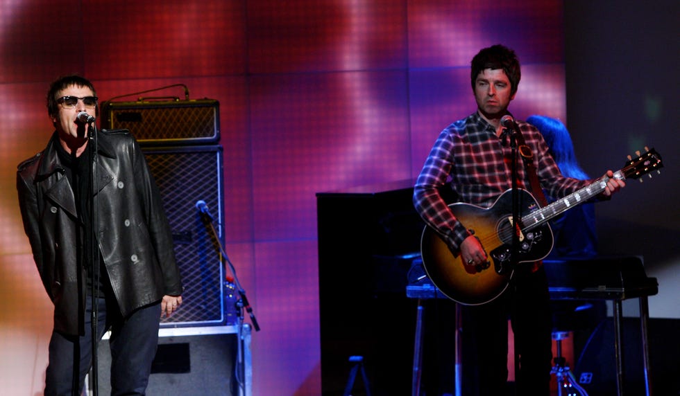 noel gallagher sings during an oasis concert as liam gallagher plays the guitar to his right