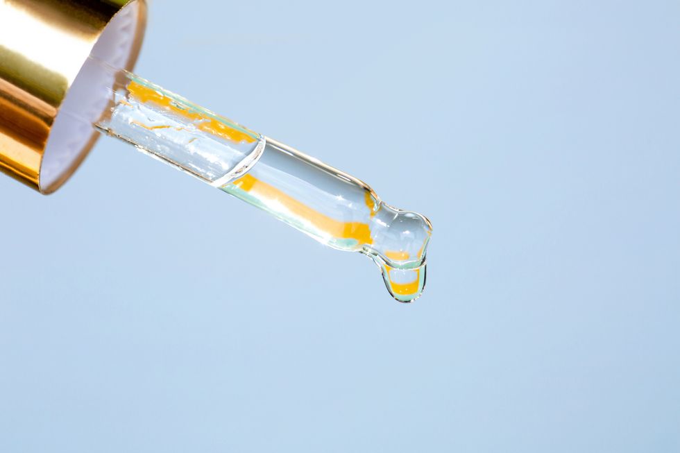 face serum is dripping from glass pipette on blue background concept of beauty procedures and body care polyglutamic acid is a new hyaluronic acid macro photography