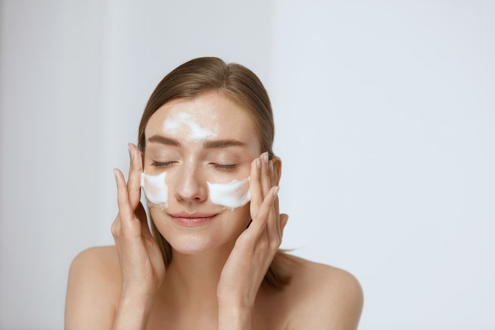Face skin care. Woman applying facial cleanser on face closeup