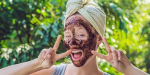 Face Skin Scrub. Portrait Of Sexy Smiling Female Model Applying Natural Coffee Mask, Face Scrub On Facial Skin. Closeup Of Beautiful Happy Woman With Face Covered With Beauty Product. High Resolution