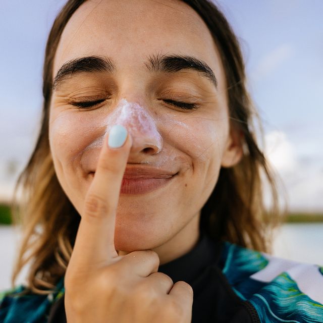 woman applying sunscreen to nose at beach