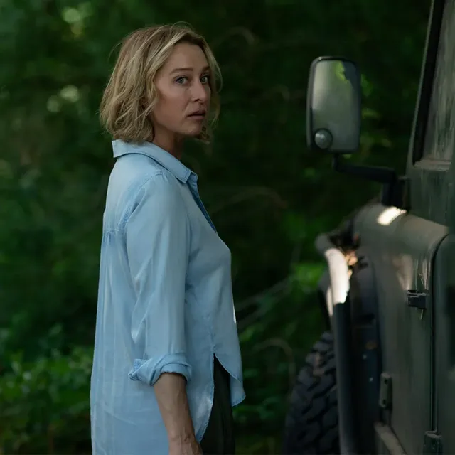 a person stands next to a dark vehicle in a forested area
