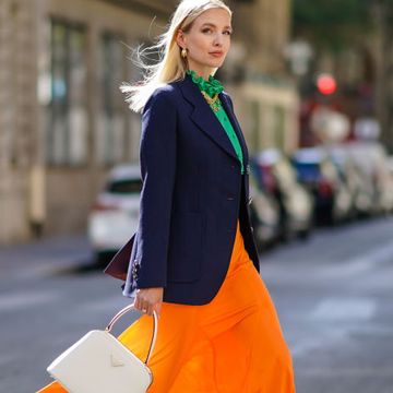 paris, france july 12 leonie hanne wears golden earrings, a golden necklace, a dark navy blue prada blazer jacket, a green ruffled silky prada shirt with frilly collar, a neon orange flowing prada skirt, a white leather prada bag, prada white shoes, on july 12, 2020 in paris, france photo by edward berthelotgetty images