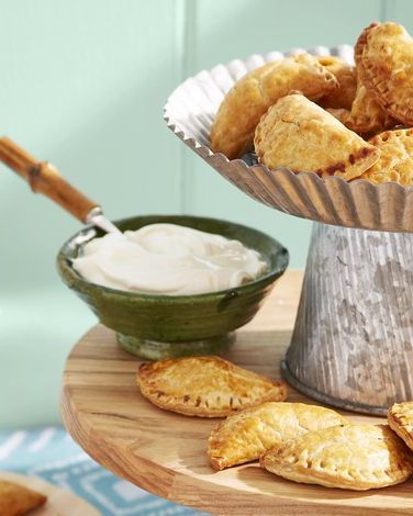 beef and raisin empanadas arranged on a wooden serving stand with a small bowl of sour cream