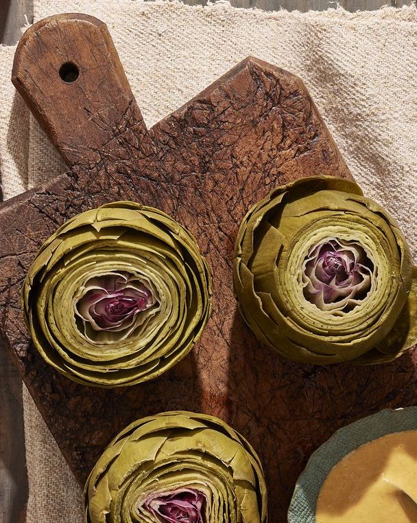 steamed artichokes on a wooden cutting board with a small bowl of smoked paprika aioli