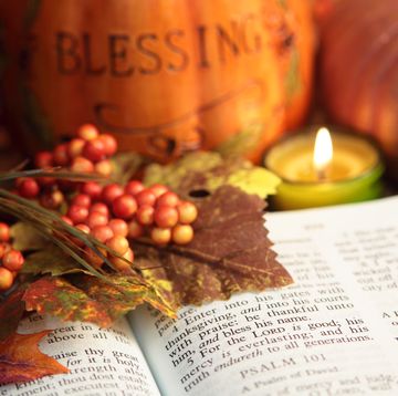 open bible showing scripture surrounded by autumn colored berries, leaves, candles, and pumpkins