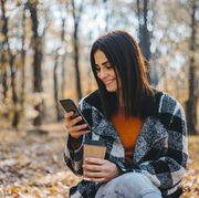 woman smiling and looking at her phone while holding a coffee