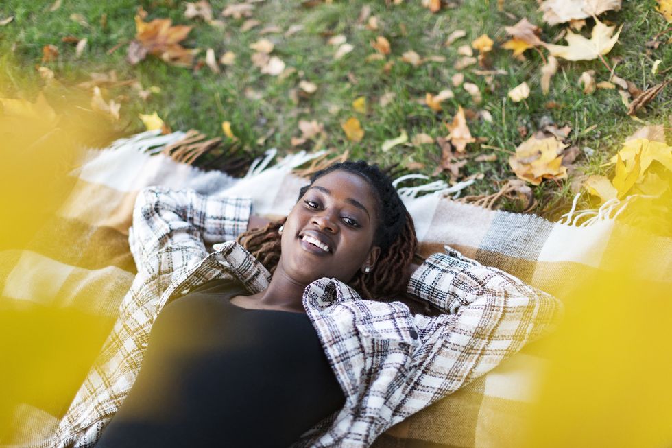 young adult black female lying down on picnic blanket amid autumn leaves that you might caption for instagram happy fall yall