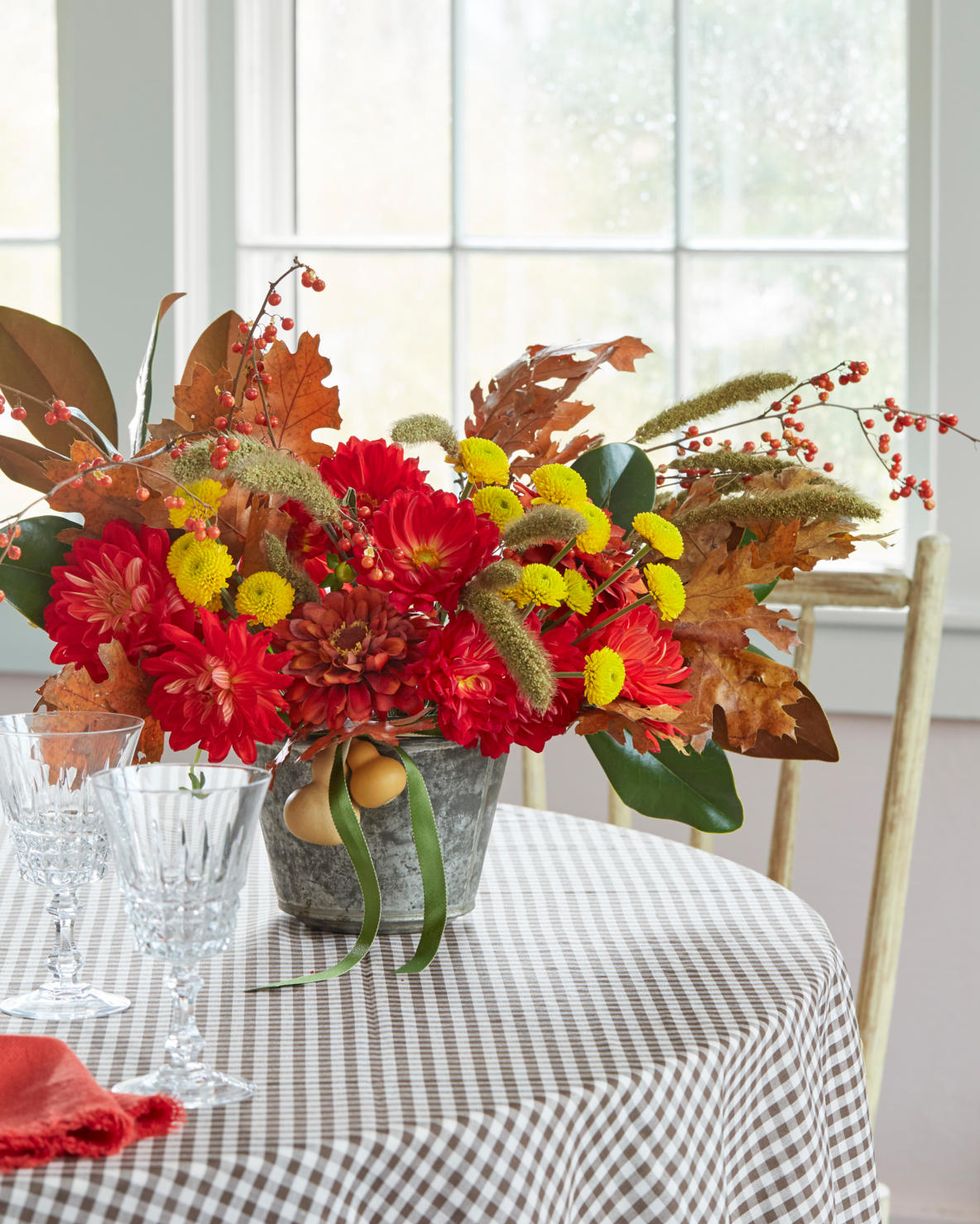 bold red and yellow blooms in a galvanized vase accented with fall leaves and berries