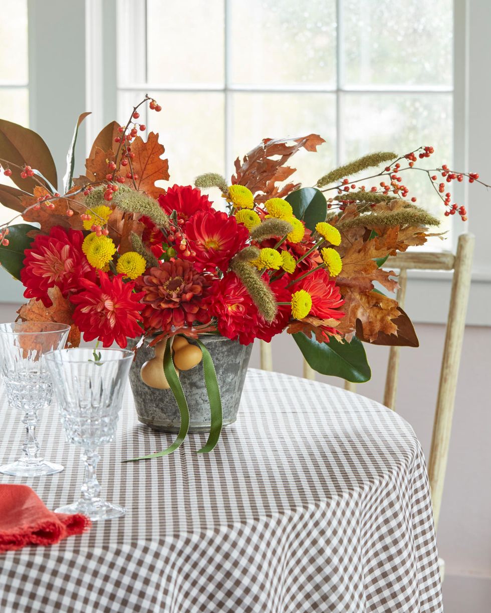 bold red and yellow blooms in a galvanized vase accented with fall leaves and berries