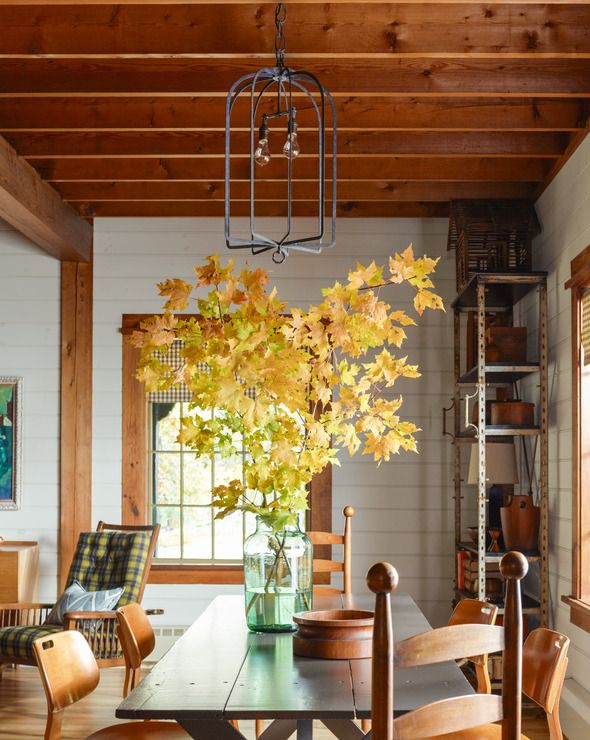 a dining room with wood furniture and a super tall arrangement of golden fall leaves