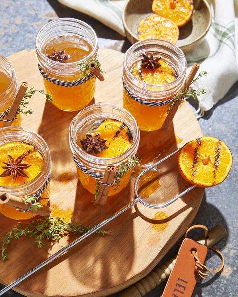 fall cocktails hot toddies in mason jar glasses with a charred orange slice and star anise on top and a cinnamon stick and sprig of thyme on the side for garnish