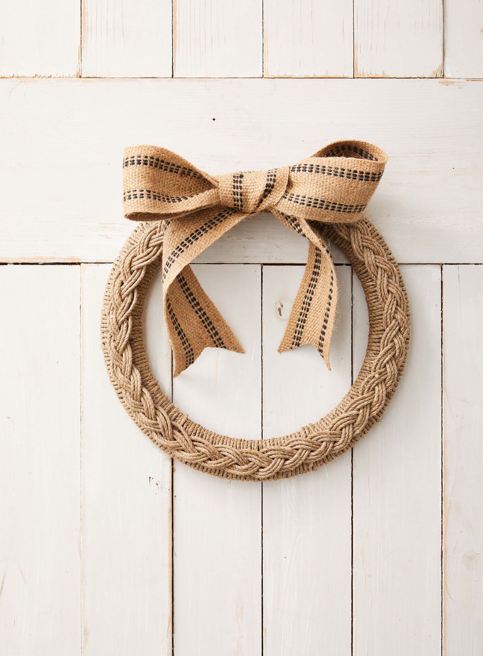 a wreath made from a wreath form that has been wrapped in thick twine topped with braided twine and finished off with a upholstry tape ribbon