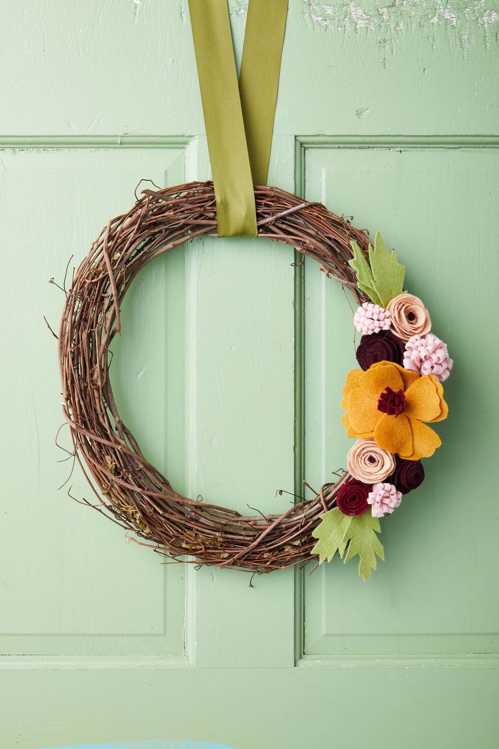 felt flowers on a grapevine wreath form hung on a green door