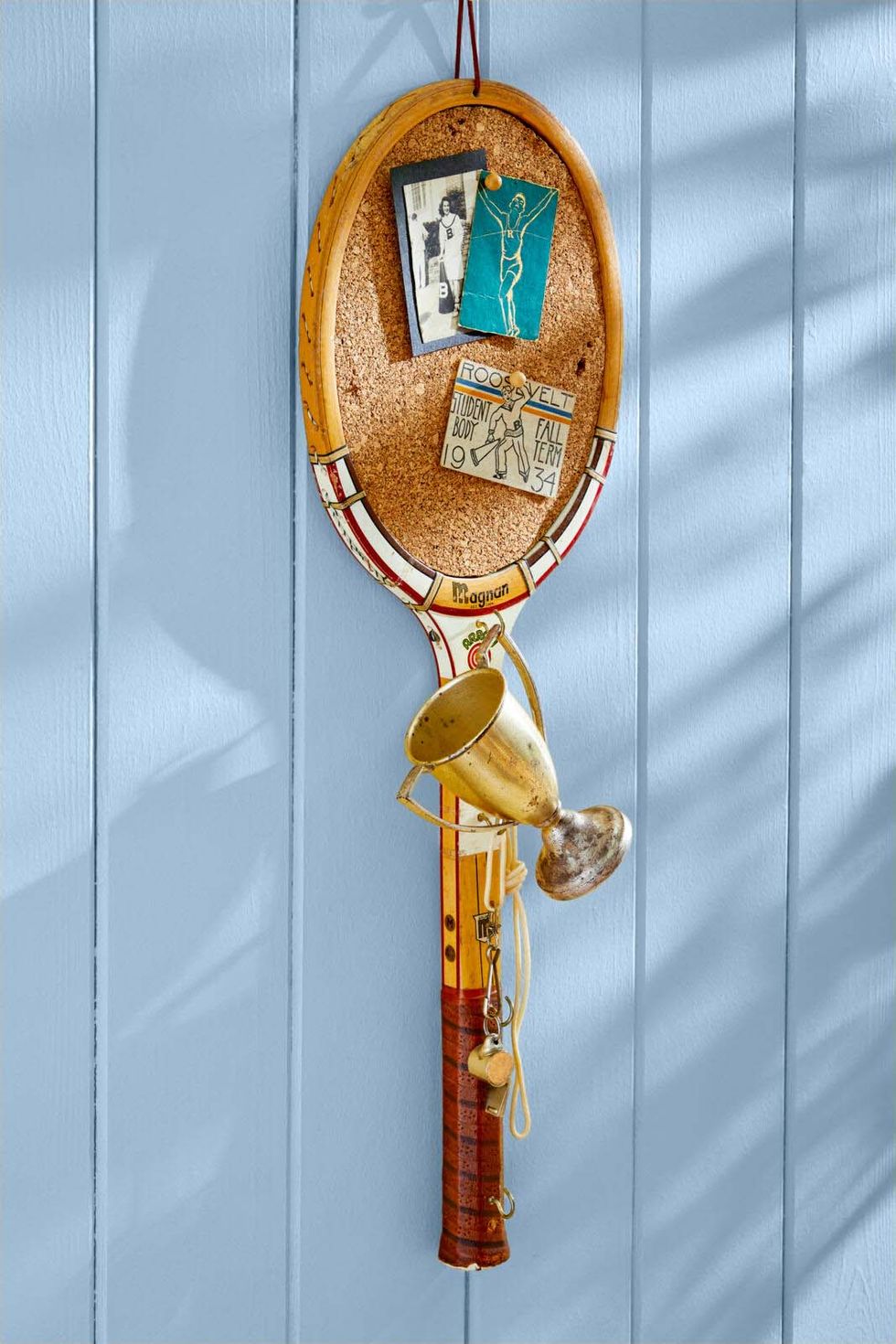 vintage tennis racquet turned into a pin board hanging on a light blue wall