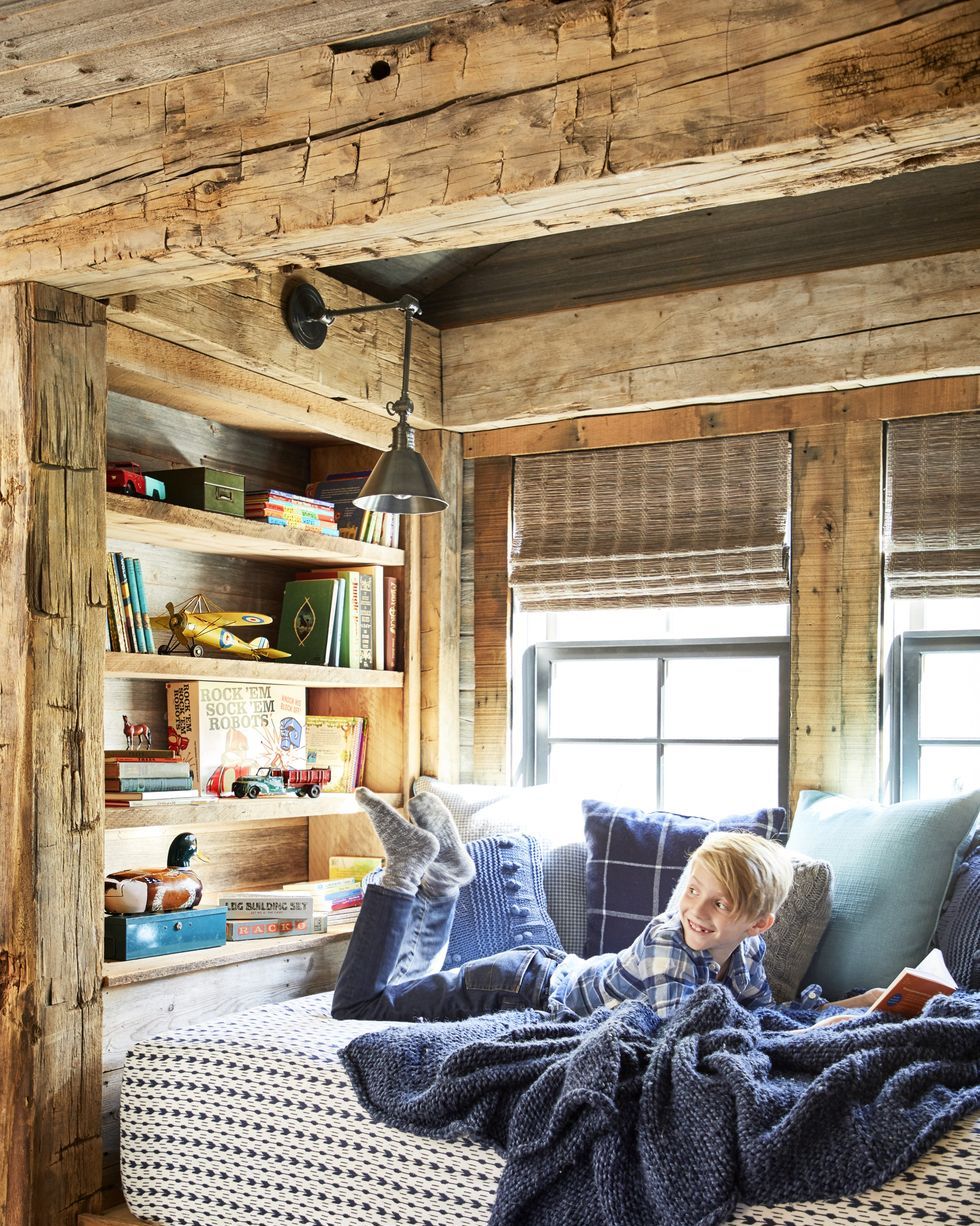 a little boy reads a book in a wood lined cubby with a navy blanket