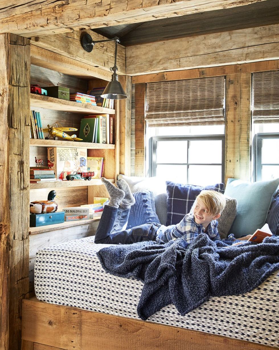 a little boy reads a book in a wood lined cubby with a navy blanket