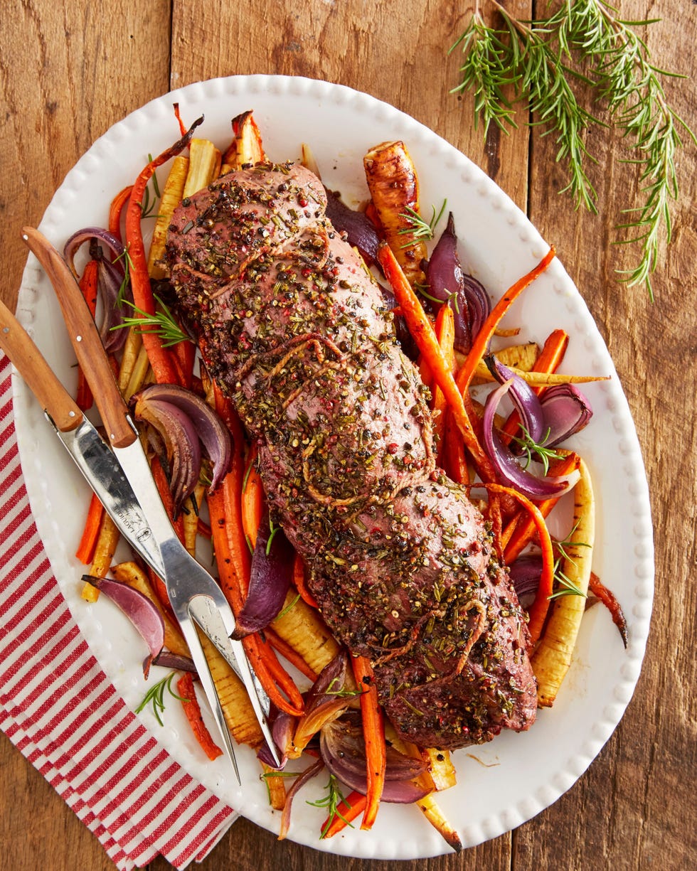 rosemary beef tenderloin with root vegetables on an oval serving plate with serving utensils