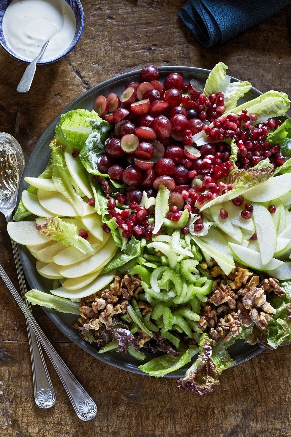 a waldorf salad arranged in a dark gray bowl with utensils to the left side on a wooden table surface