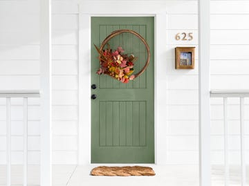 green front door with wreath made of grain sifter and fall foliage