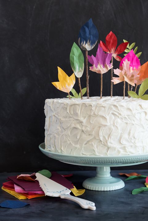 cake topper crafted from twigs and painted paper cutouts of fall leaves, atop white cake on blue pedestal