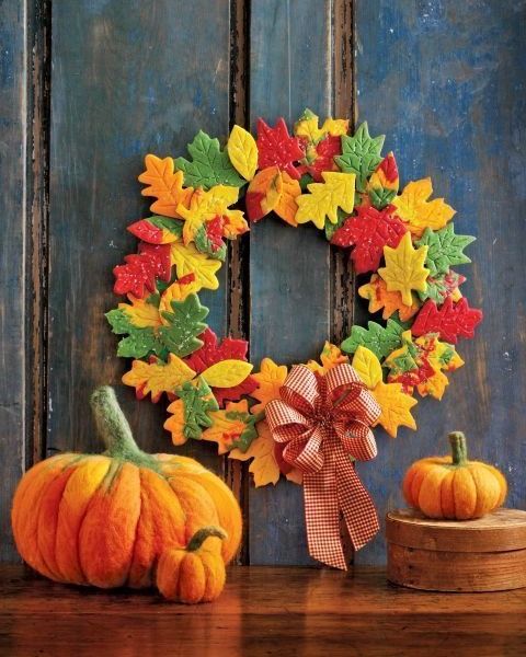 wreath made from colorful leaf shaped cookies, pictured on rustic blue washed panel wall above yarn pumpkins