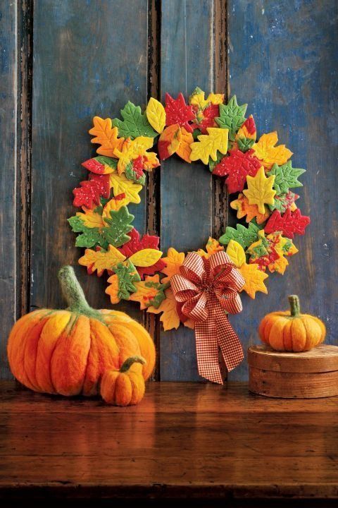 wreath made from colorful leaf shaped cookies, pictured on rustic blue washed panel wall above yarn pumpkins