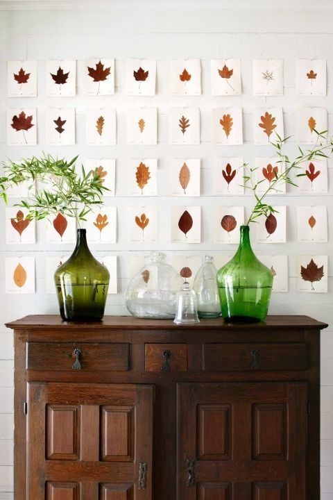 40 small prints of individual fall leaves hung in 8x5 grid on white wall, above wood chest topped with decorative bottles