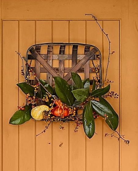 fall wreath crafted from old tobacco basket, magnolia leaves, and pumpkins on orange door