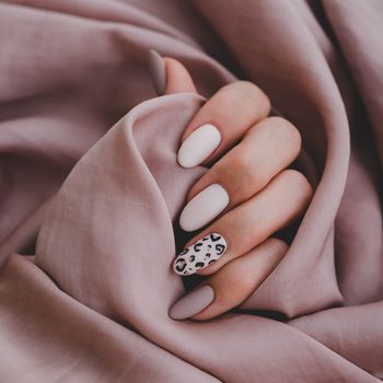 womans hand with a beautiful oval shaped manicure autumn trend, beige color polishing with leopard pattern on nails with gel polish, shellac