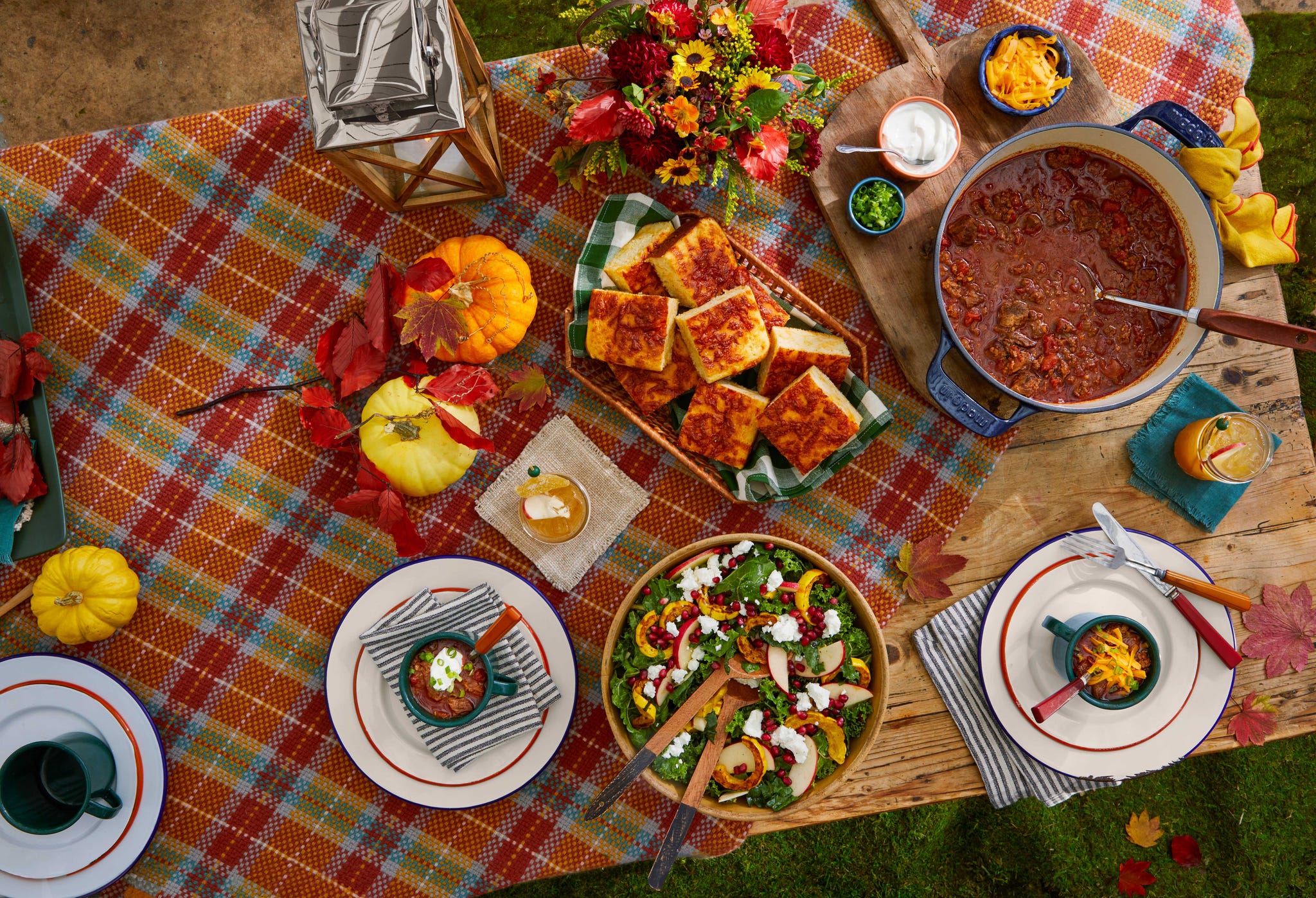 a table set outside with a white tablecloth and blankets on the chairs