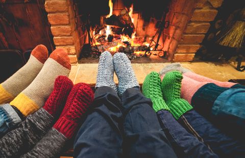 View of legs of happy family in warm socks in front of fireplace in winter, love and cozy concept, focus on gray woolen socks in center
