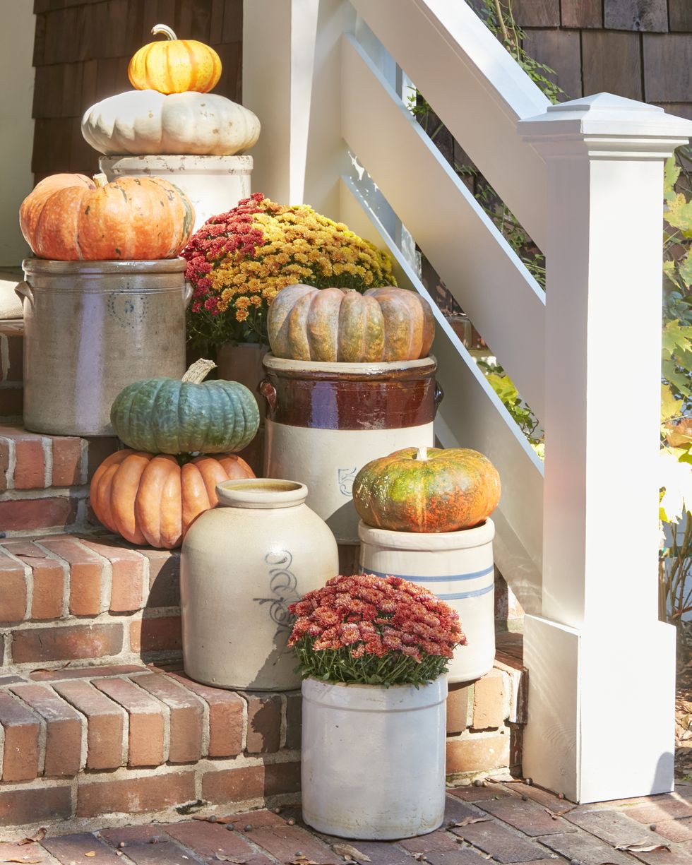 display of flat and wide pumpkins on top of an assortment of crocks staggered on a stoop or front stairs
