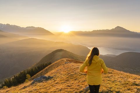 rear view of woman with yellow jacket gazing at mountains and northern branch of lake como at dawn peglio, como province, lombardy region, italy