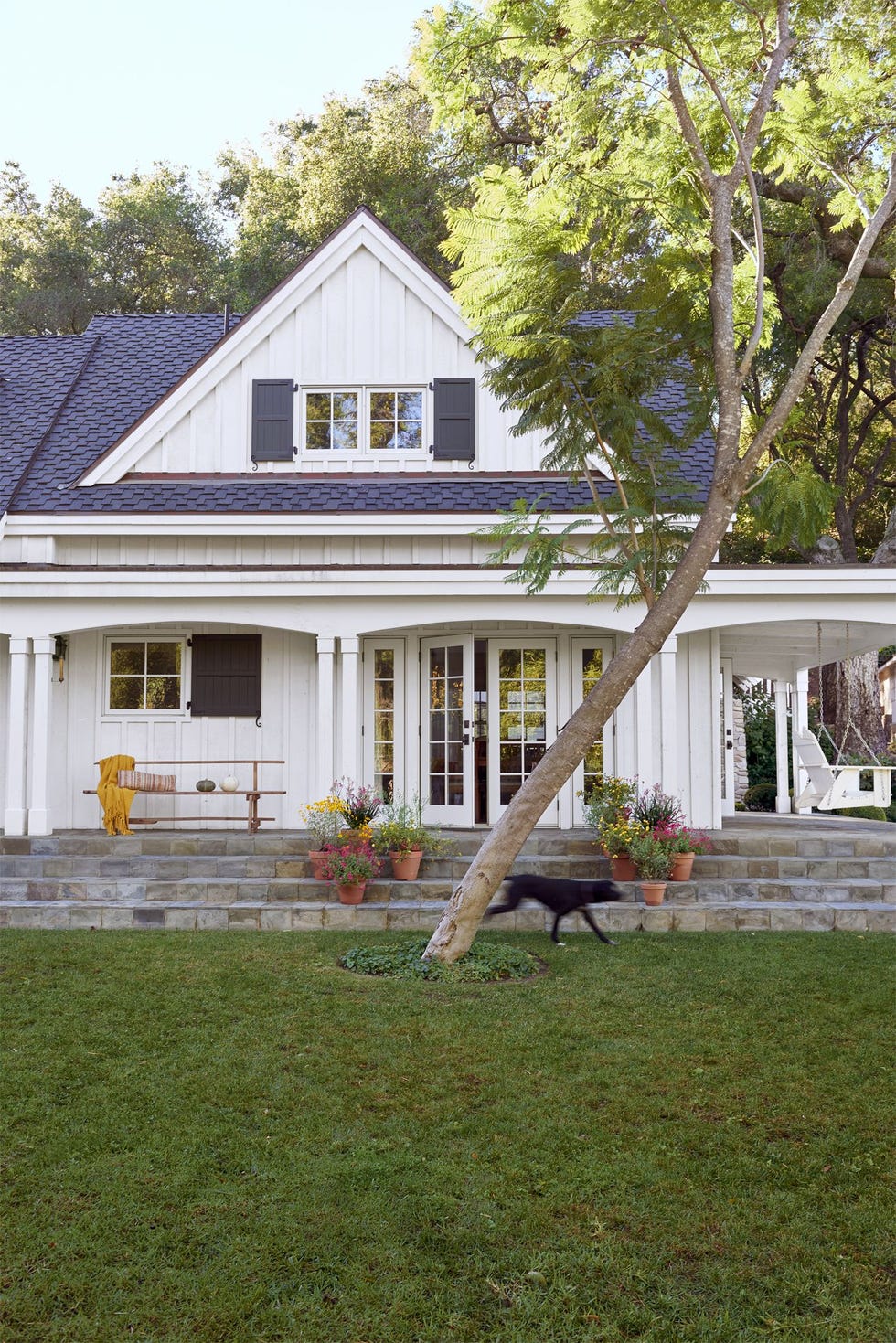 terra cotta pots of fall blooms and bench with yellow throw blanket decorate stone front porch of white cape cod style house