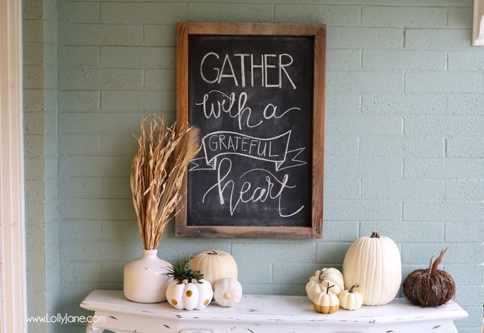 fall porch display with pumpkins on console table and chalkboard sign that reads gather with a grateful heart